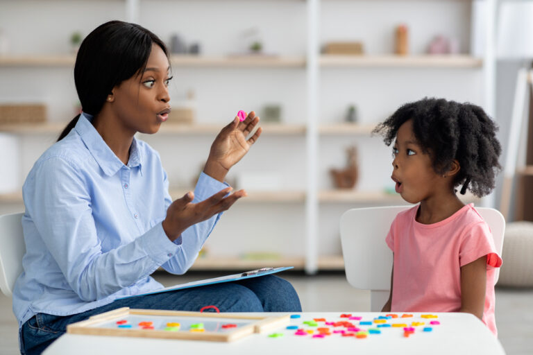 Female speech therapist mouthing a word for a young girl to repeat.