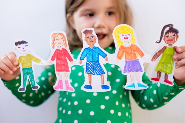 child holding cutouts of images of various people, which will be used in a pragmatics teaching activity.