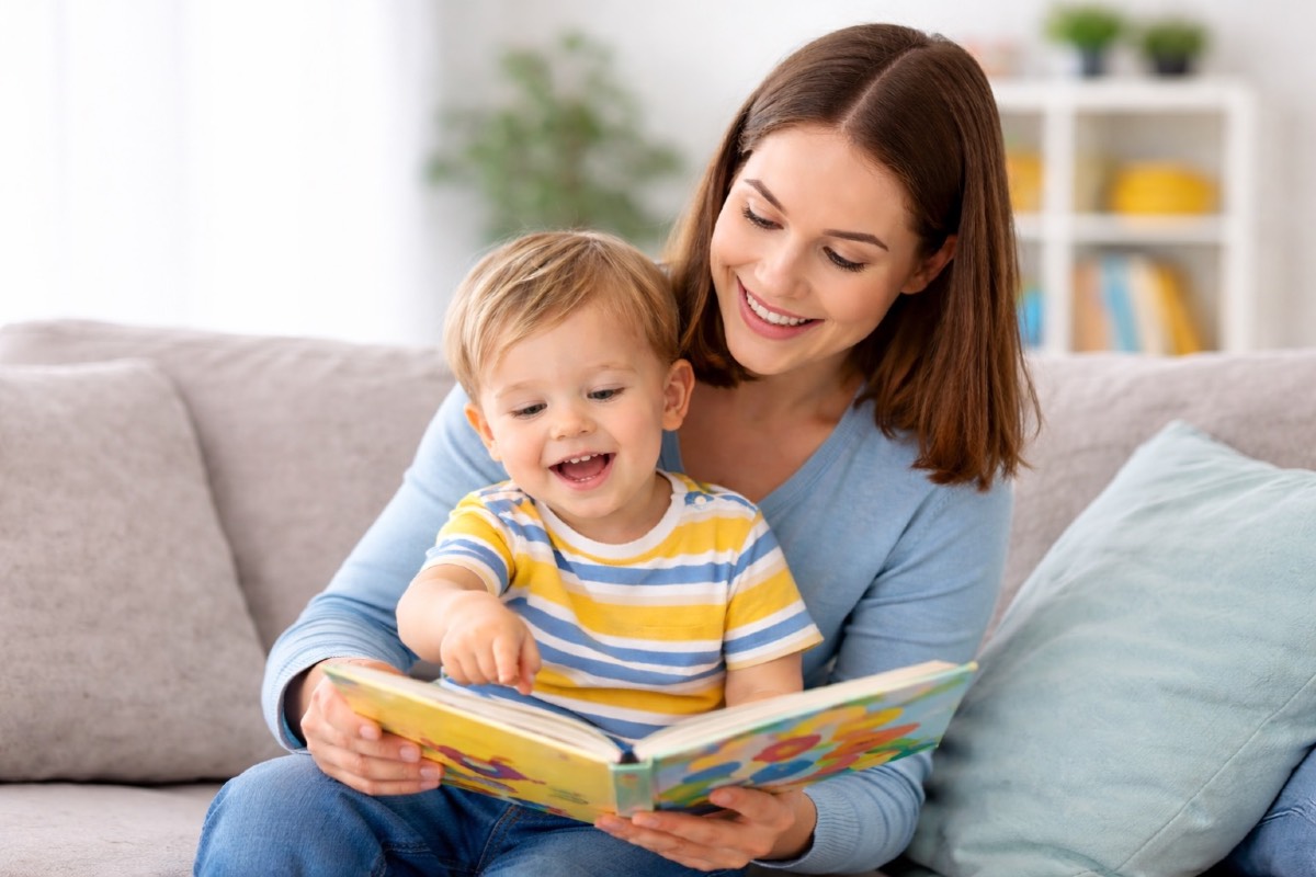 Toddler pointing at a book while engaging with a caregiver — an early communication milestone.